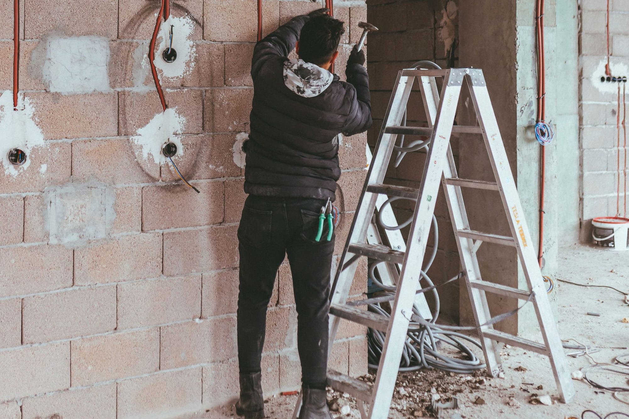 Monteur installiert Leerrohre in einer Ziegelwand im Rohbau, daneben eine Leiter.
