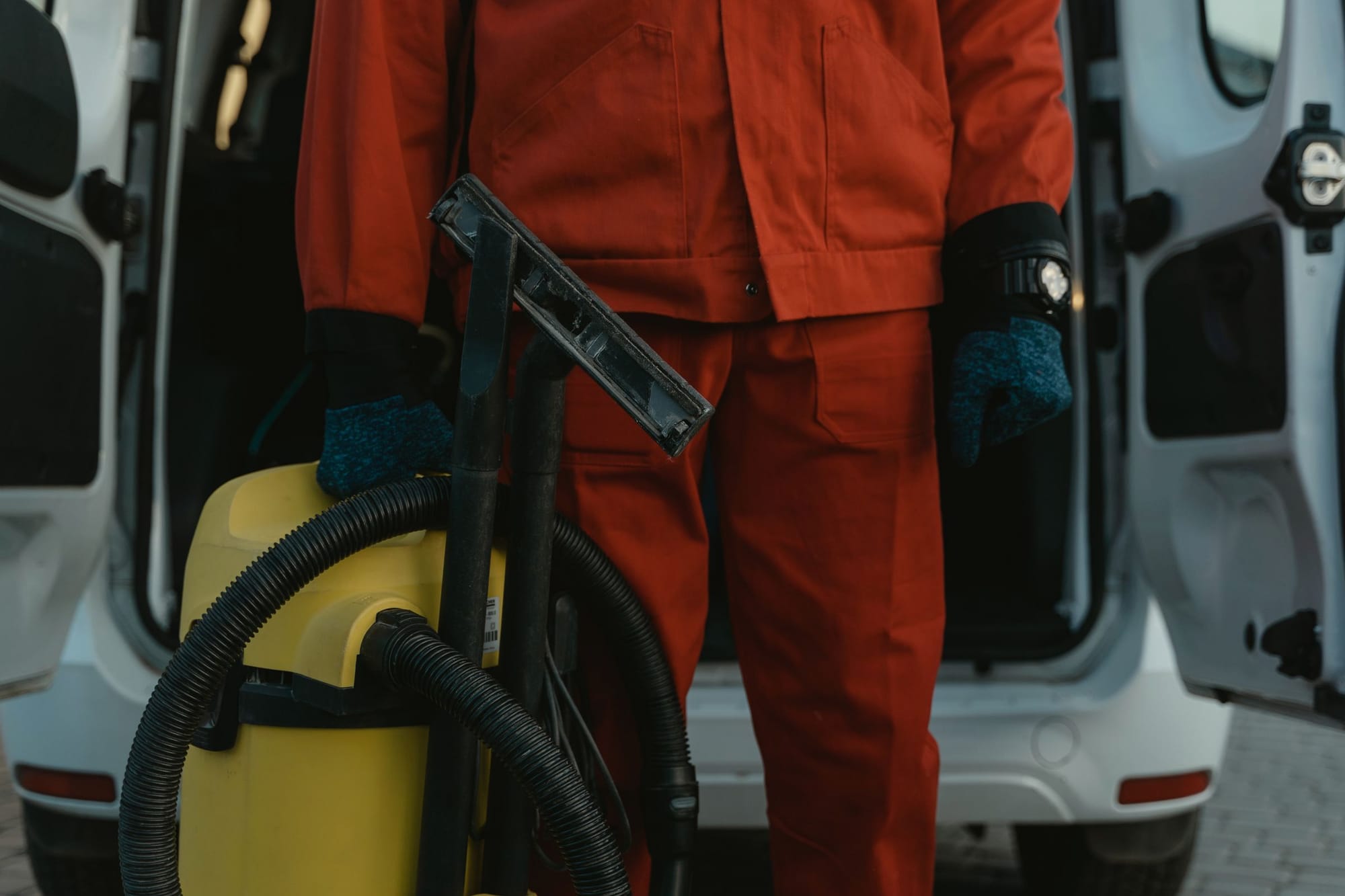 Reinigungskraft in Arbeitskleidung mit Nasssauger vor dem offenen Transporter.
