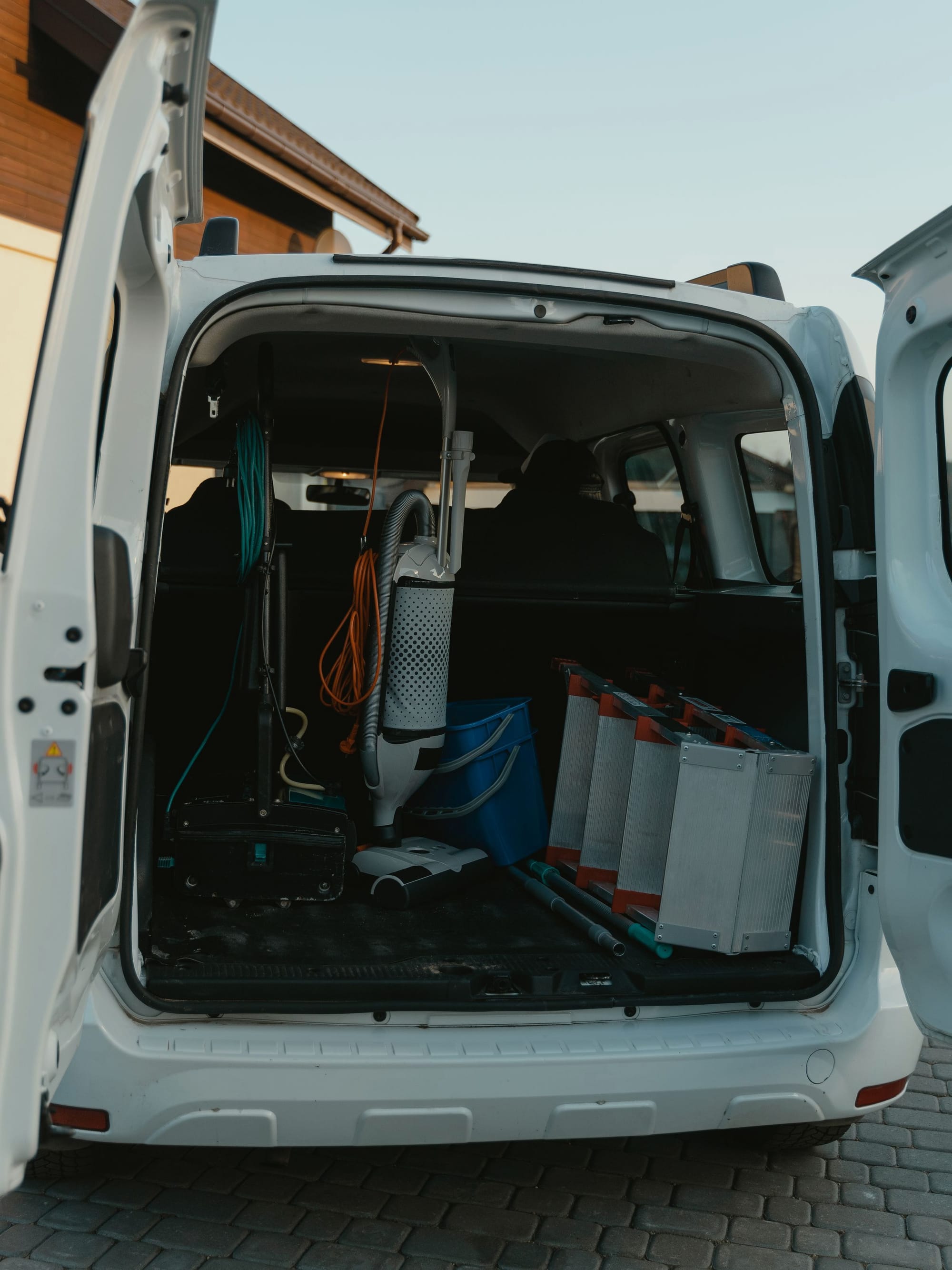 Offene Hecktür eines weissen Transporters auf einem Pflasterhof, im Laderaum Gerät und Kisten vom Tag.